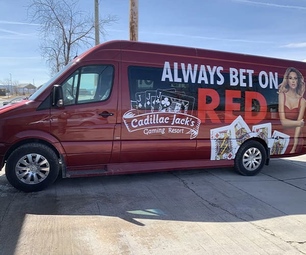 Custom Vinyl Vehicle Graphics for Cadillac Jack's gaming resort van with a woman in a red dress, always bet on red text and four jack poker cards.